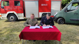 Komendat KP PSP i komendant WSP Pomiechówek podpisują porozumienie, w tle wóz strażacki