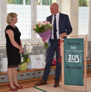 dwie osoby stoją na sali gimnastycznej, osoba po prawej trzyma bukiet kwiatów