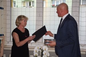 dwie osoby kobieta i mężczyzna, kobieta przyjmuje teczkę gratulacyjną od mężczyzny