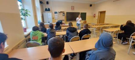 na fotografii młodzież siedzi i słucha prowadzącej w ramach warsztatów