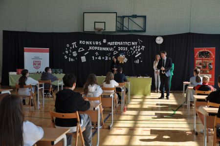 sala gimnastyczna, dyrektor wita uczestników, dzieci siedzą przy pojedynczych ławkach