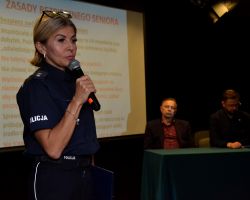 pani policjant trzyma mikrofon, w tle ekran, po prawej stronie wicestarosta nowodworski i burmistrz