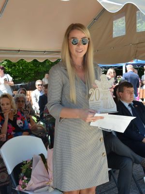 Radna Powiatu Nowodworskiego Aleksandra Szczurowska na tle pozostałych gości, trzyma w ręku drewnianego aniołka
