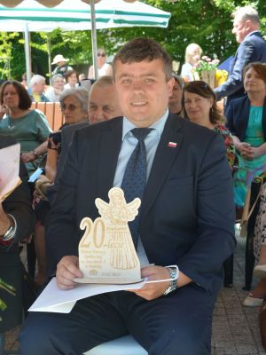 Przewodniczący Rady Powiatu Nowodworskiego Marcin Gągolewski siedzi i trzyma podziękowania- drewnianego aniołka