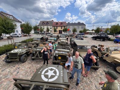 samochody jeep willys zaparkowane, obok uczestnicy wydarzenia