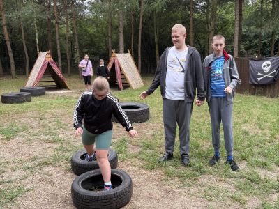 gry i zabawy uczestników półkolonii, w tle las, dziewczynka przechodzi z opony do opony