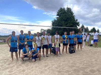 uczestnicy wydarzenia stoją na boisku do gry w siatkówkę plażową i trzymają puchary