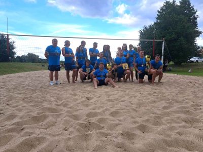 uczestnicy wydarzenia stoją na boisku do gry w siatkówkę plażową i trzymają puchary