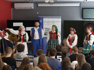 grupa osób w polskich strojach ludowych przed szkolną publicznością