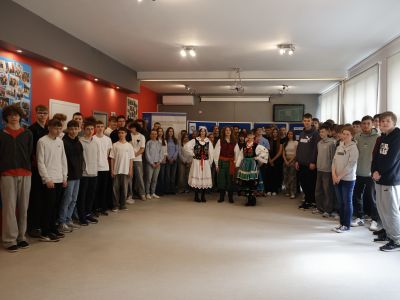 uczniowie stoją na korytarzu szkolnym, a w centrum trzy osoby w strojach ludowych