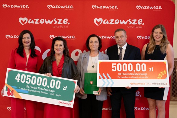Starosta, Wicestarosta, Skarbnik Powiatu, Członkini Zarządu oraz przedstawiciel Młodzieżowej Rady Powiatu na tle ścianki Mazowsza, prezentujący symboliczne czeki z kwotą przyznanego wsparcia.